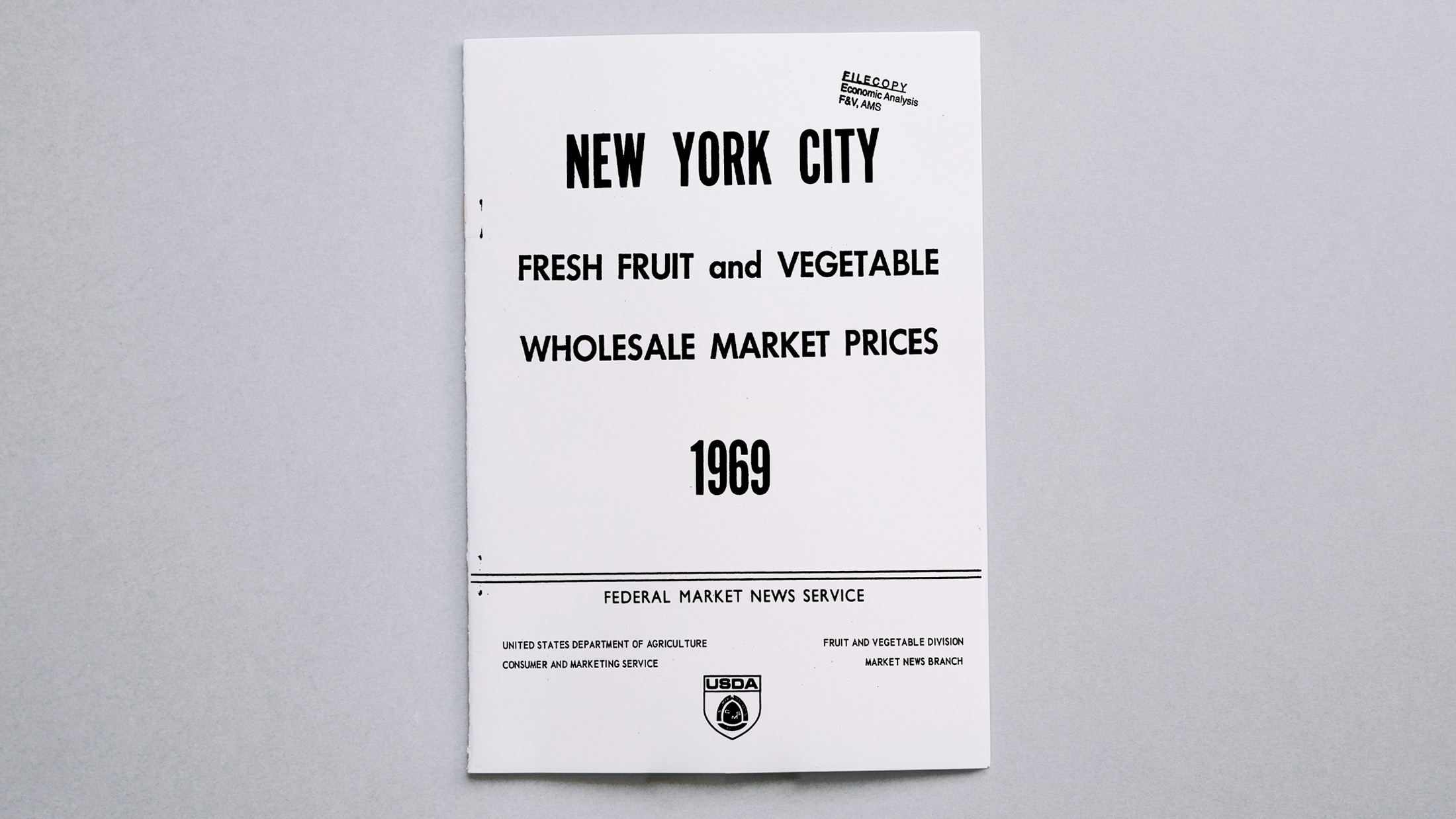 A white USDA pamphlet on a gray background stating New York City Fresh Fruit and Vegetable Wholesale Market Prices 1969