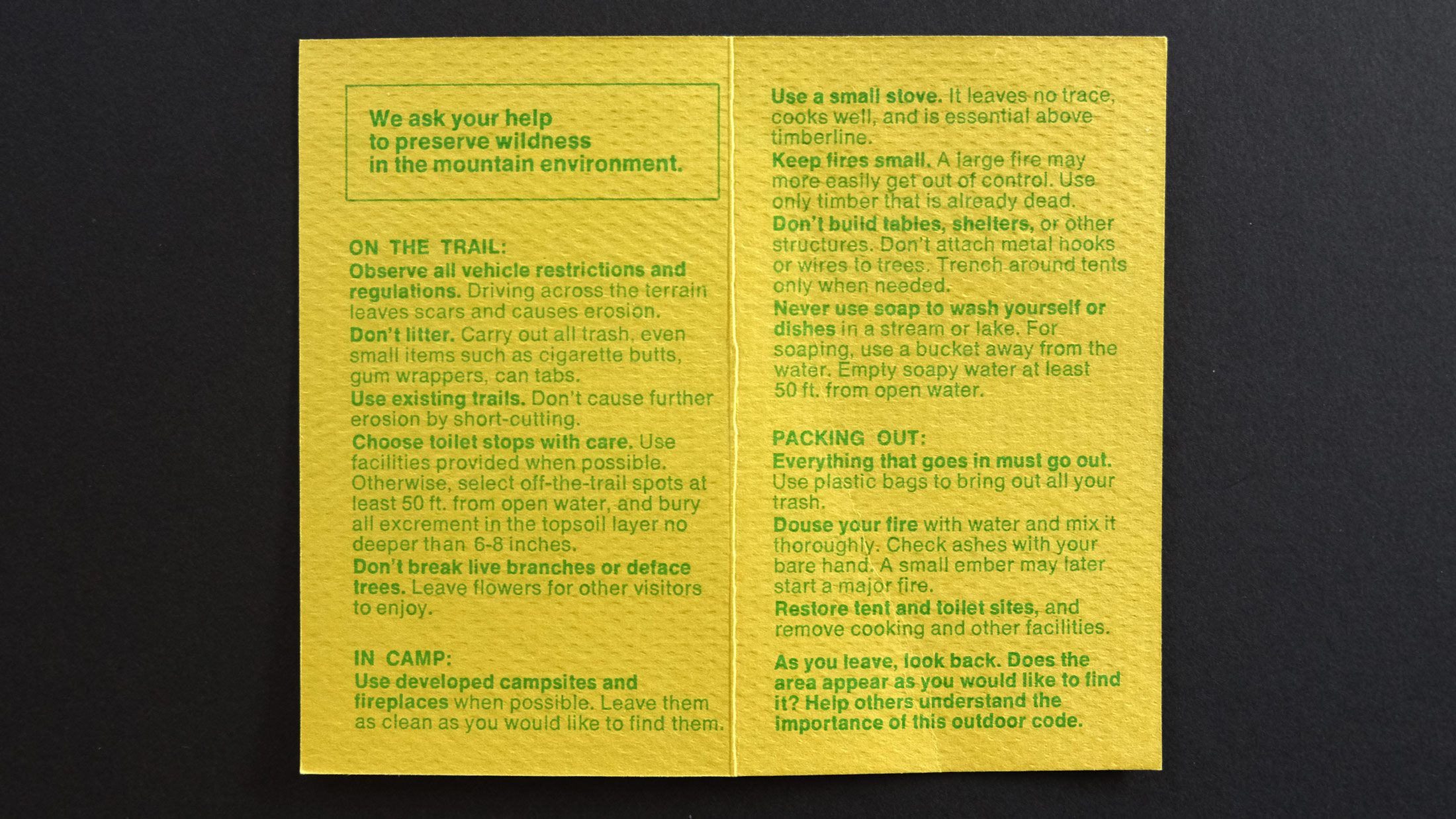 A yellow Forest Service pamphlet has blocks of green text explaining best practices for taking care of the forest and trail while backpacking