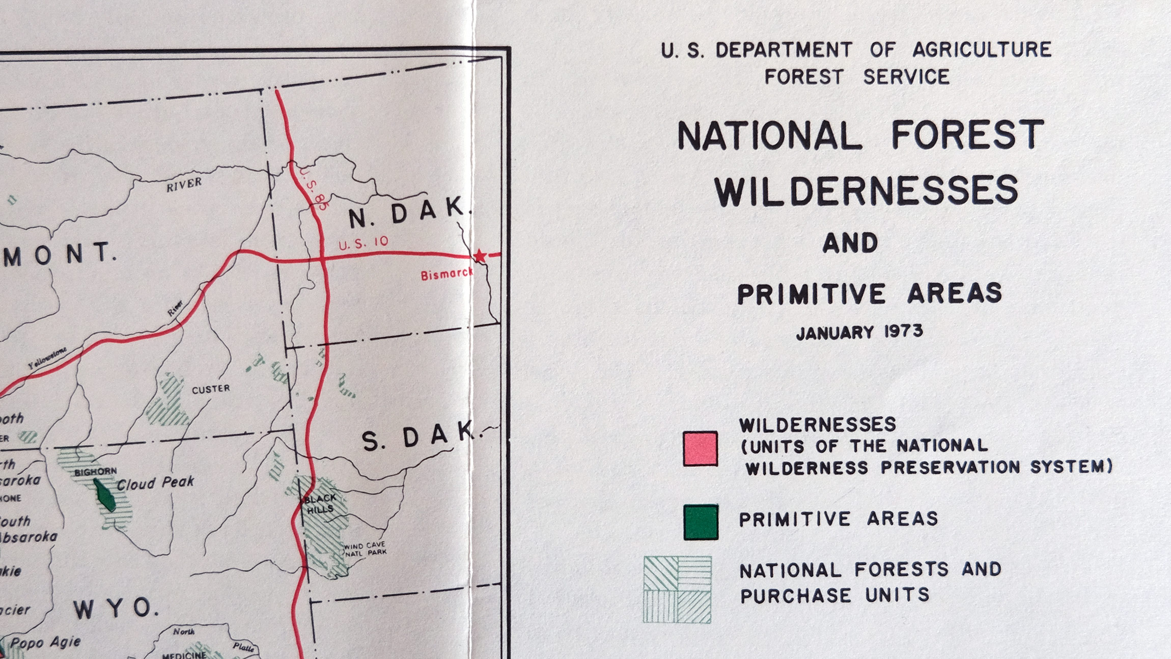 A vintage Forest Service fold out pamphlet shows "National Forest Wildernesses and Primitive Areas" in black all caps sans-serif font on white paper above a colorful map key and to the right of a cropped map area of the mid west states