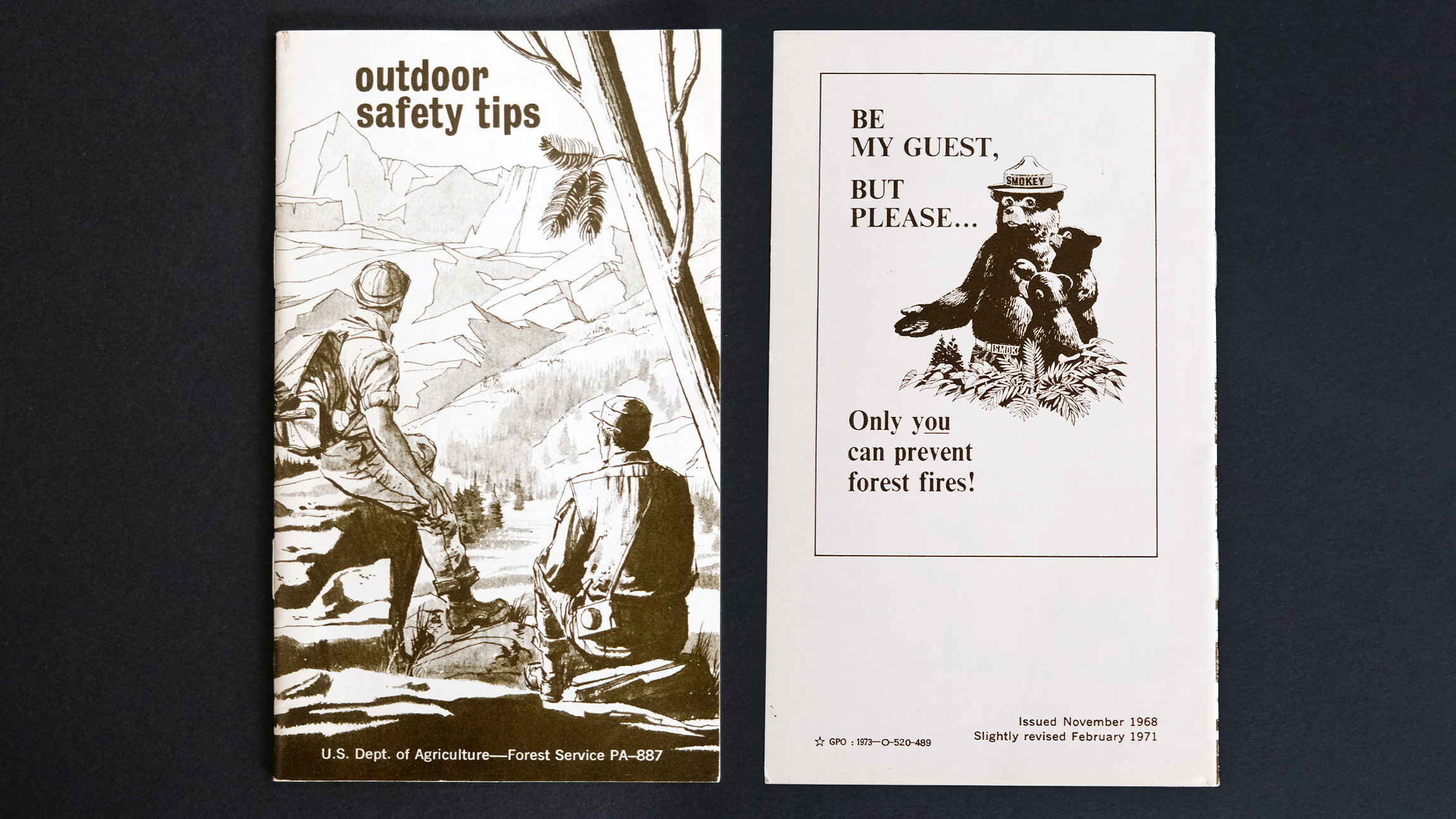 The front and back of a small vintage Forest Service pamphlet is seen that says outdoor safety tips, with two illustrated hikers looking at a mountain vista, and on the back is Smokey Bear giving us a forest fire prevention message as usual